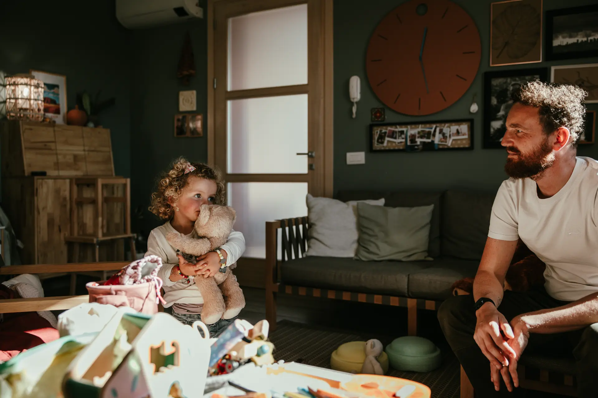 Momento spontaneo di vita quotidiana tra padre e figlia con orsetto di peluche in soggiorno, fotografia lifestyle di famiglia di Sara Mellerio.