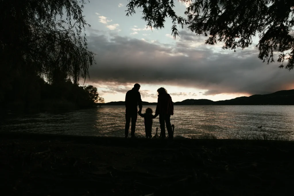 famiglia-03-26-6 Silhouette di una famiglia di tre persone in riva al lago al tramonto con alberi in cornice, fotografia di famiglia suggestiva di Sara Mellerio.