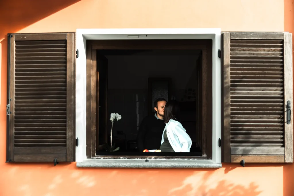 Coppia in attesa che si bacia alla finestra di una casa colorata – Servizio fotografico di maternità di Sara Mellerio