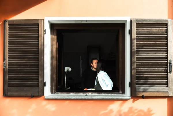 Coppia in attesa che si bacia alla finestra di una casa colorata – Servizio fotografico di maternità di Sara Mellerio