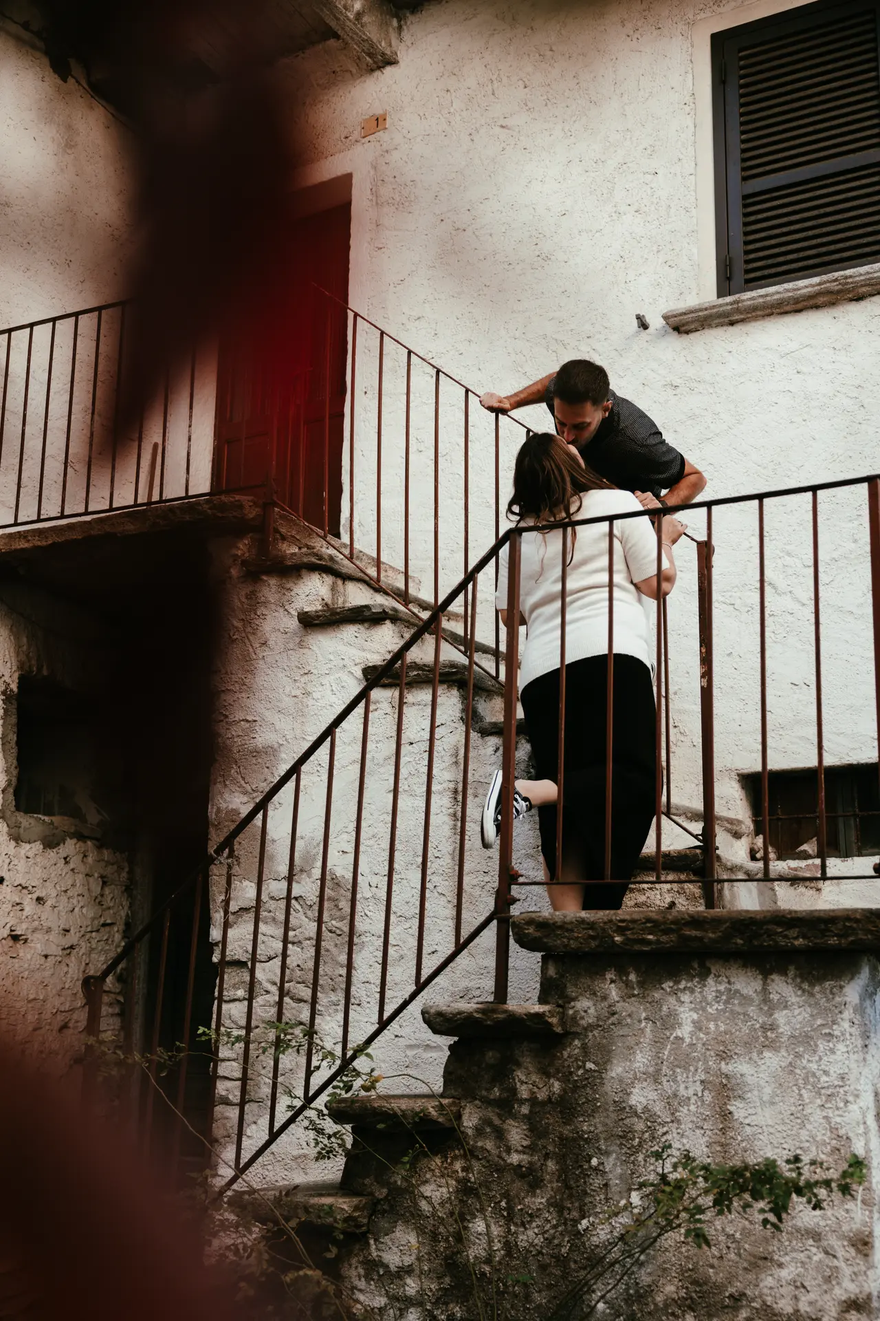 Coppia in attesa si bacia su una scala antica in pietra, fotografia di gravidanza in stile reportage di Sara Mellerio.