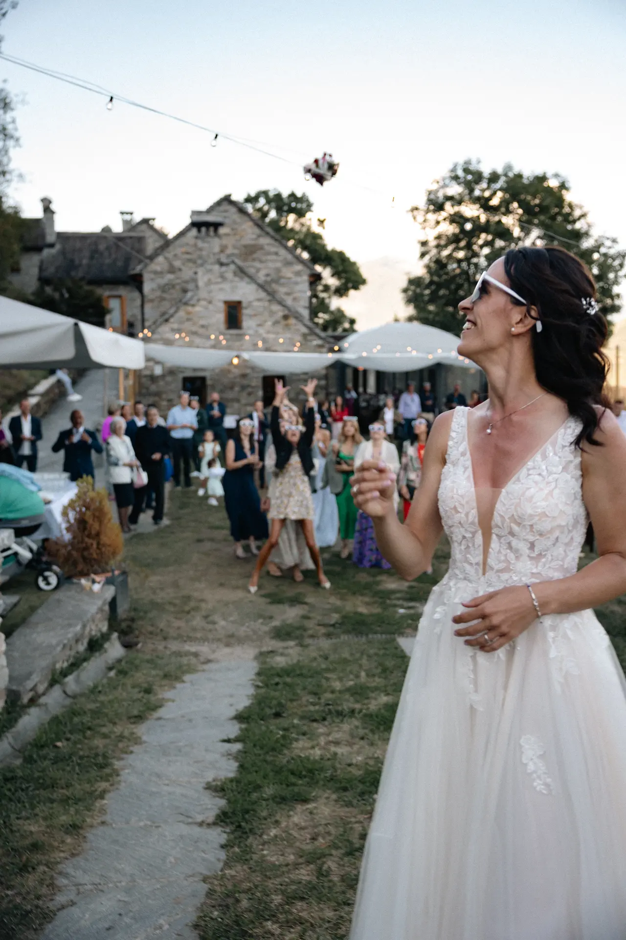 Momento del lancio del bouquet della sposa durante il ricevimento all'aperto al tramonto, scatto di Sara Mellerio.