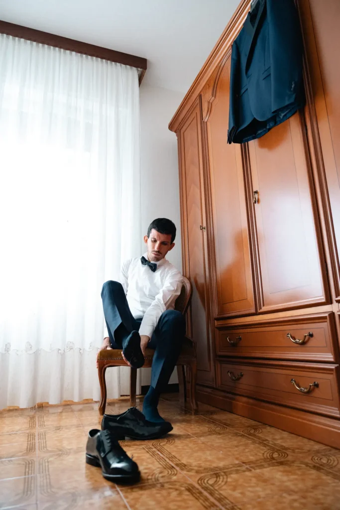 matrimoni-03-26-2 Lo sposo si prepara indossando le scarpe eleganti in camera da letto, fotografia documentaria di matrimonio di Sara Mellerio.