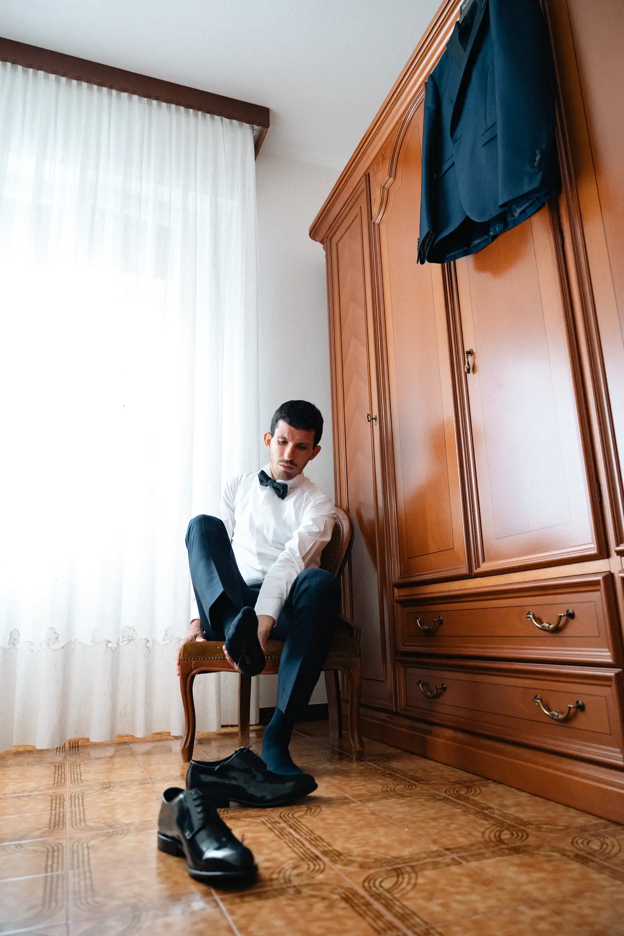 Lo sposo si prepara indossando le scarpe eleganti in camera da letto, fotografia documentaria di matrimonio di Sara Mellerio.